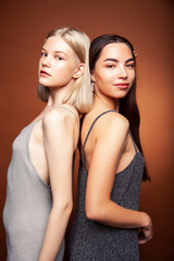 two pretty diverse girls happy posing together: blond and brunette on brown background, lifestyle people concept