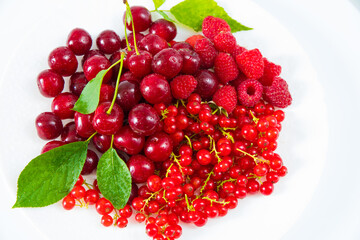 Assorted red fresh berries on a plate on a white background.