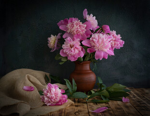 A bouquet of peonies stands in a clay jug on a wooden table.