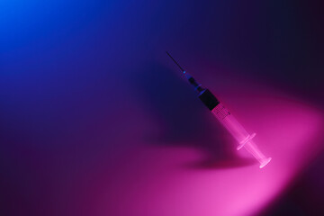 Close-up of a sterile full of blood syringe in colored ambulance light at night. Blue and pink...