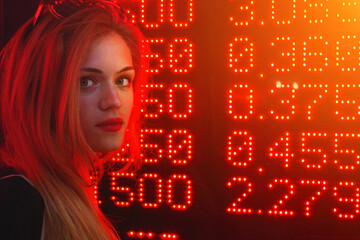 Young caucasian woman standing near a currency exchange board on a city street.