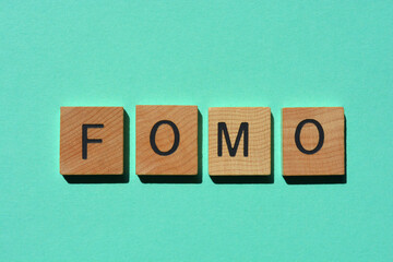 fomo, in acronym for Fear of Missing Out in wooden alphabet letters isolated on tyrquoise background