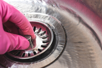 Woman in pink glove plugs cork in sink for dishwashing. Save water