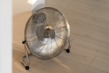 Silver metal ventilation fan on wooden floor at home. 