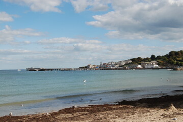 Small Seaside Town and Pier in Dorset England UK Beach and Water View with Village Houses in Background on Sunny Summer Day with Blue Sky and White Clouds