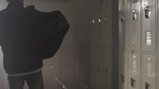 Fighter walks into gym changing room with big dufffle bag placing it on the ground and opening locker