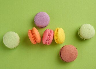 baked multi-colored macaroon cookies lie in a row on a green background
