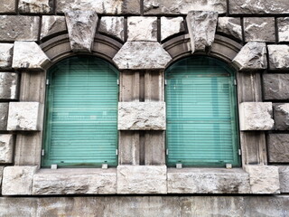 Rundbogenfenster mit leuchtend grünen Jalousien als Sonnenschutz in einer Fassade aus massivem...