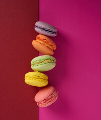 baked multi-colored macaroon cookies lie in a row on a pink red background