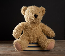 brown teddy bear sits on a brown wooden table, behind an empty black chalk board