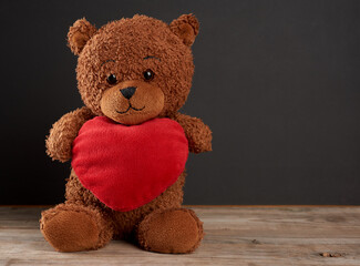 cute brown teddy bear holding a big red heart and sits on a black wooden background