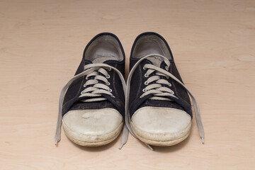Old dirty shabby sneakers over light wooden background