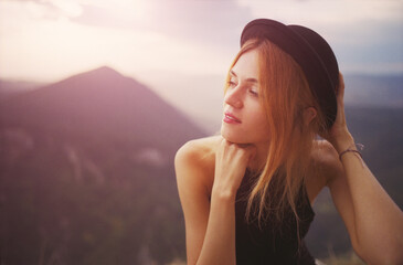 Close-up of a young Caucasian woman in a black dress and black hat on a sunset background high in the mountains of Bulgaria. Real grain scanned film.