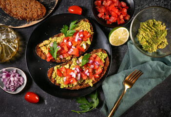 Top view of delicious mashed avocado sandwiches with cooking ingredients on black background