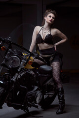 Fototapeta na wymiar Young, long hair white skinned latina woman wearing makeup, black bra, shorts, leggings and leather boots, on yellow motorcycle, studio with black background