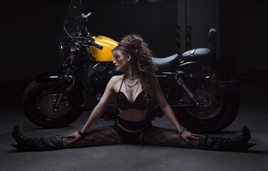 Obraz na płótnie Canvas Young Latin woman with thin white skin with long hair collected and jewelry, wears black clothing, uses a bra, shorts, fishnet mesh and boots, sitting next to a yellow motorcycle with her legs open 