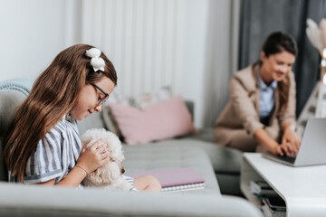 Beautiful young mother working from home while her daughter watching online school class. Social distancing and Covid-19 or Coronavirus lifestyle.