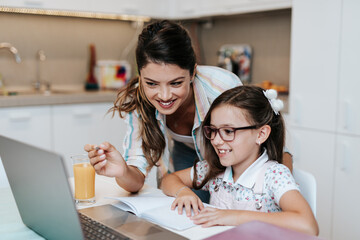 Beautiful young mother helping her younger daughter with homework.