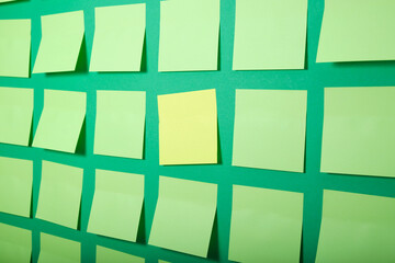 one yellow sticker and many light green sticky notes on a green background, selective focus