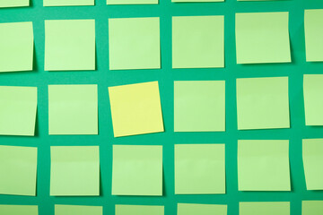 one yellow sticker and many light green sticky notes on green background, brainstorming and teamwork concept