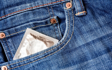 A condom pops out of the front pocket of a pair of jeans. Prevention of sexually transmitted...