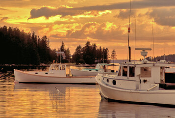 Sky and clouds illuminated by warm golden sunset with lobster boats anchored in quiet cove near...