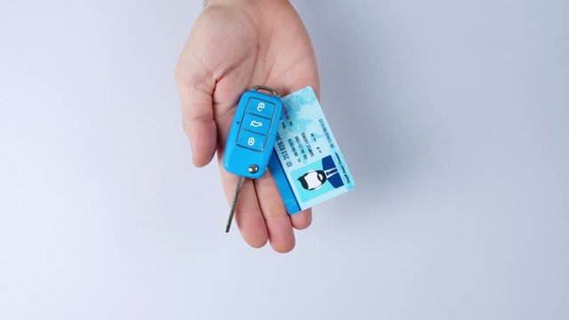 Male hand with driving license and car key on light background, top view