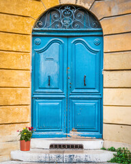 Bright blue old wooden residential door in orange building on city street in France