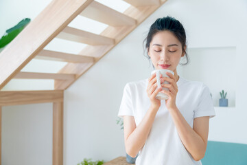 Young asia woman with ponytail in white t-shirt holding a cup of coffee or tea relaxing at home in...
