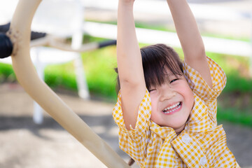 Obraz premium Happy kid hanging out with exercise machines on playground. Asian girl wearing yellow shirts are happy sweet smiling. Healthy child is 5 years old. Close up.