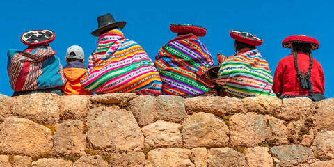 Peruvian Quechua indigenous people in traditional clothing on an Inca wall in Chinchero, Cusco, Peru. - obrazy, fototapety, plakaty