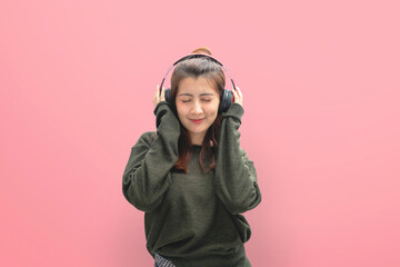 Beautiful young woman in headphones listening to music and dancing on pink background.