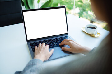 Mockup image of a businesswoman using and typing on laptop keyboard with blank white desktop screen in the office