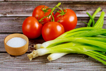 Tomatoes and chives with salt on wooden table.