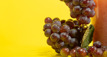 Bunches of pink grape and juice on yellow background