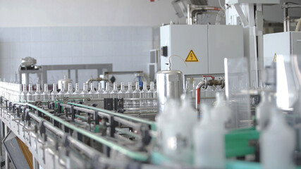 Factory for bottling alcoholic beverages. Working machine with several conveyor lines at time for production of vodka. Glass bottles in conveyor belt in distillery production line.