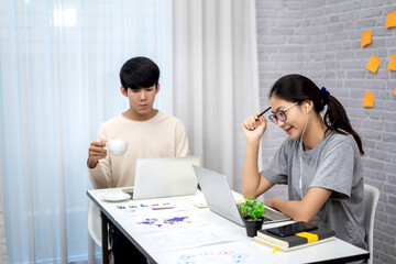 Two young asian in casual clothes talking and discussing working with laptop at home.