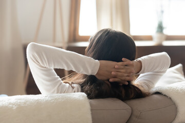 Back rear head shot peaceful young woman leaning on cozy couch, enjoying stress free leisure...