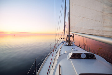 White yacht sailing in an open sea at sunset. Close-up view from the deck to the bow. Clear blue...