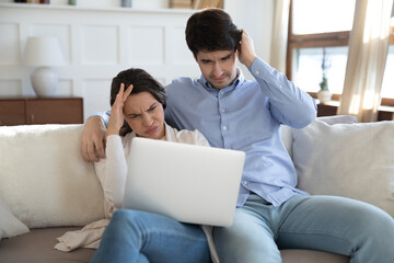 Fototapeta premium Stressed confused unhappy young family couple looking at laptop screen, feeling depressed of with bad news banking notification, received eviction notice email or having tech computer problems.