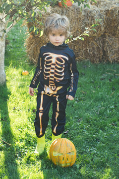 Halloween skeleton child. Child play outdoors. Cheerful child and pumpkin on sunshine background. Happy little boy.