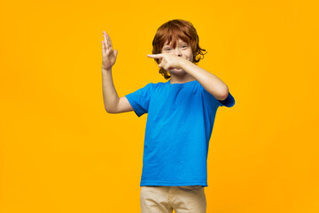 The red-haired boy shows his palm and gestures with his hands on a yellow background