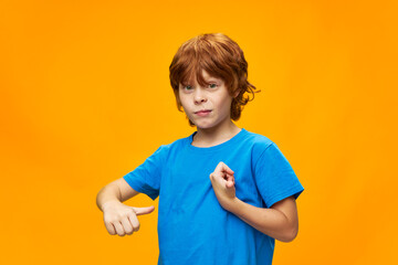 A boy with freckles shows his thumb to himself and a blue t-shirt 