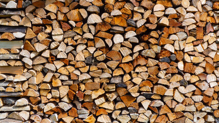 Firewood cut and stacked. Wall of wooden pieces. Warm colors with shades of brown. Wood stacked with precision. Wooden natural cut logs texture background
