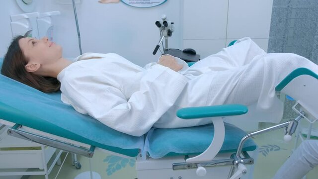 Young patient woman in gynecological chair in clinic, side view. Modern interior in medical office. Doctor gynecologist preparing to inspection. Examination and consultation of gynecologist.