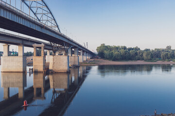 View of the bridge over the river. The structure is reflected in the water, on the other side of the river you can see the trees. There are no people. High quality photo