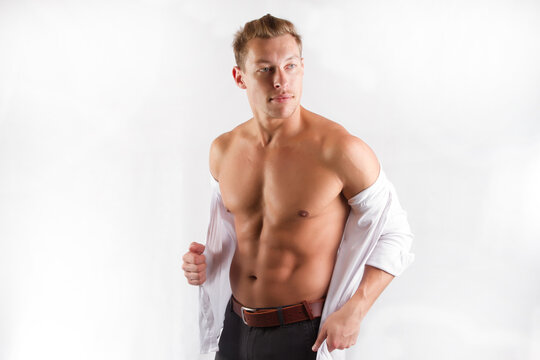 One beautiful sexy strong young man with a muscular body in gray trousers poses in a Studio on a white background.