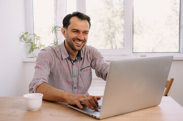 Happy smiling man in shirt with a cup of coffee works on laptop