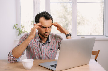 Tired man in shirt with a cup of coffee works on laptop