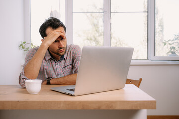 Tired man in shirt with a cup of coffee works on laptop